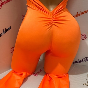 May include: A bright orange jumpsuit with a low back and a gathered detail at the back. The jumpsuit has a wide leg.
