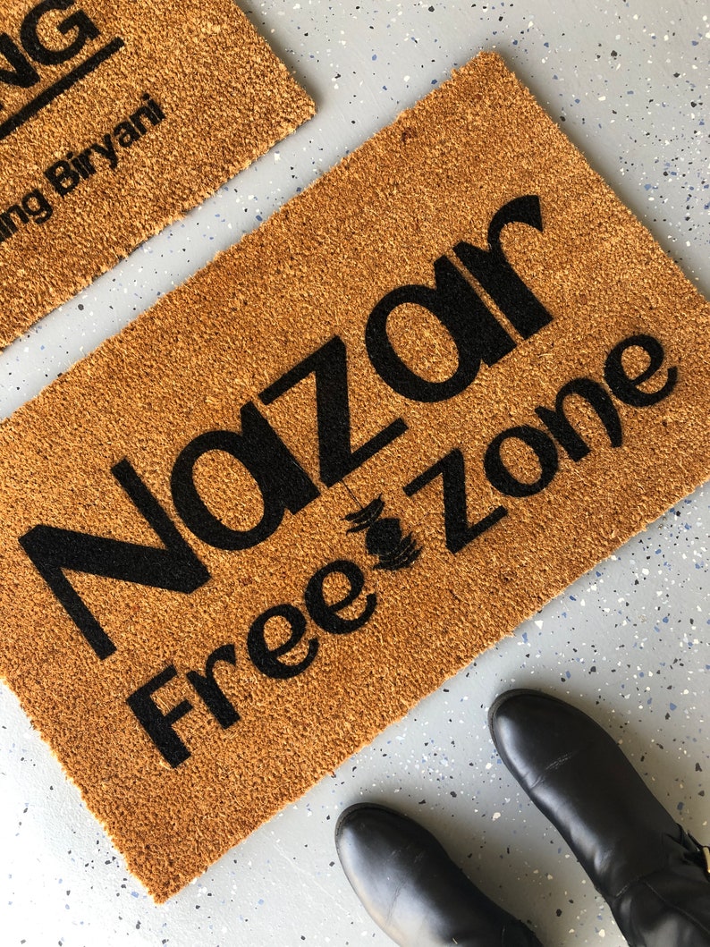 Puede incluir: Una alfombra de coco marr&oacute;n con el texto "Nazar Free Zone" en letras negras.