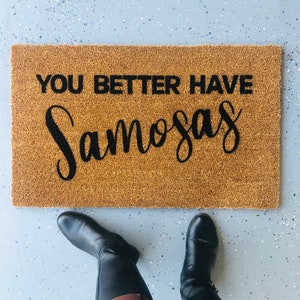 Puede incluir: Una alfombra de coco marr&oacute;n con el texto "You better have samosas" en letras negras.