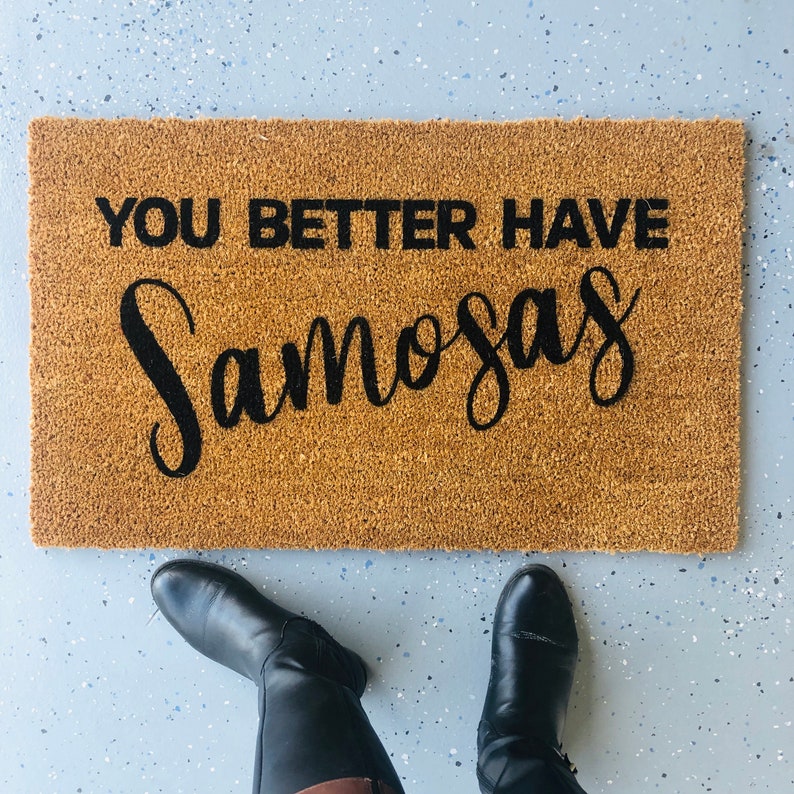 Puede incluir: Una alfombra de coco marr&oacute;n con el texto "You better have samosas" en letras negras.