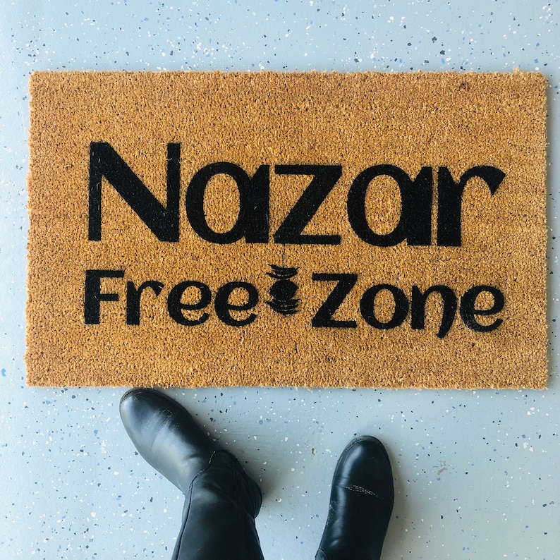 Puede incluir: Una alfombra de coco marr&oacute;n con el texto "Nazar Free Zone" en letras negras.