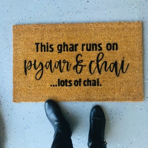 Puede incluir: Una alfombra de coco marr&oacute;n con el texto "This ghar runs on pyaar & chai...lots of chai." en letras negras.