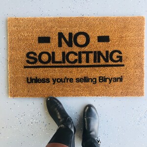 Puede incluir: Una alfombra de bienvenida marr&oacute;n con el texto "NO SOLICITING Unless you're selling Biryani" en letras negras.
