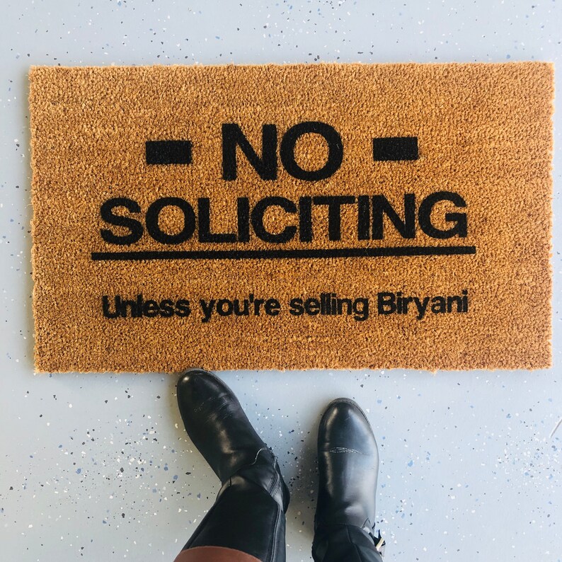 Puede incluir: Una alfombra de bienvenida marr&oacute;n con el texto "NO SOLICITING Unless you're selling Biryani" en letras negras.