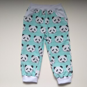Op de afbeelding: Een lichtblauwe broek met een witte tailleband en witte boorden. De broek heeft een pandabeerprint over de hele oppervlakte.