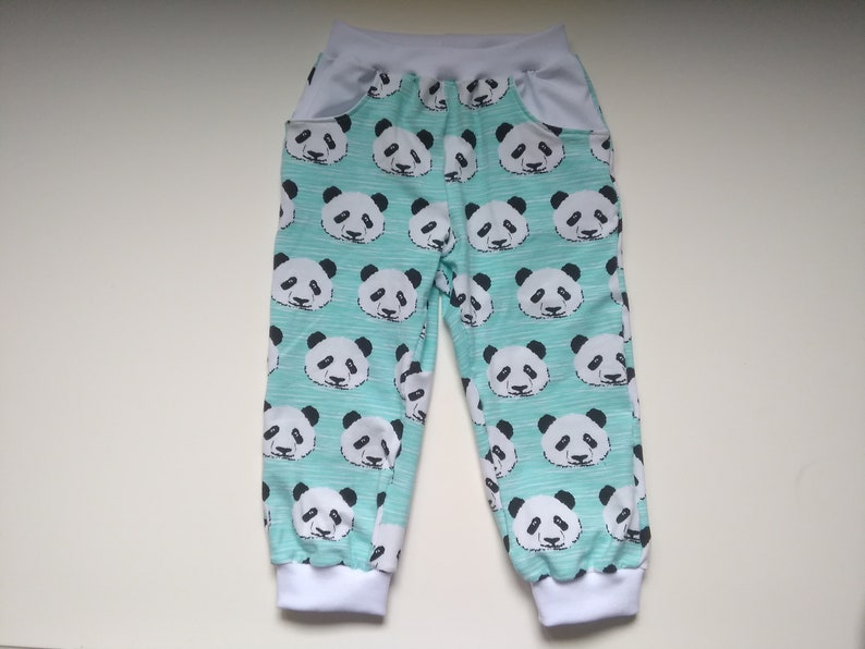 Op de afbeelding: Een lichtblauwe broek met een witte tailleband en witte boorden. De broek heeft een pandabeerprint over de hele oppervlakte.