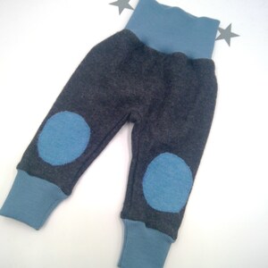Op de afbeelding: Grijze babybroek met blauwe kniepleisters en een blauwe elastische tailleband.