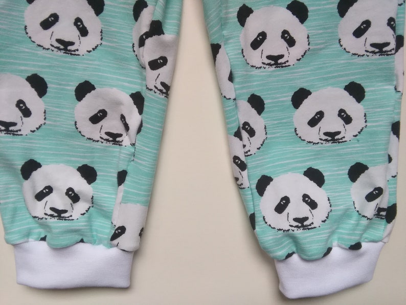 Op de afbeelding: Een paar tealblauwe sweatpants met een witte en zwarte pandabeerprint. De sweatpants hebben witte elastische boorden aan de onderkant.