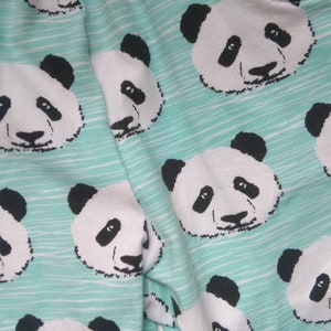 Op de afbeelding: Een turquoise stof met een herhalend patroon van zwart-witte panda gezichten.
