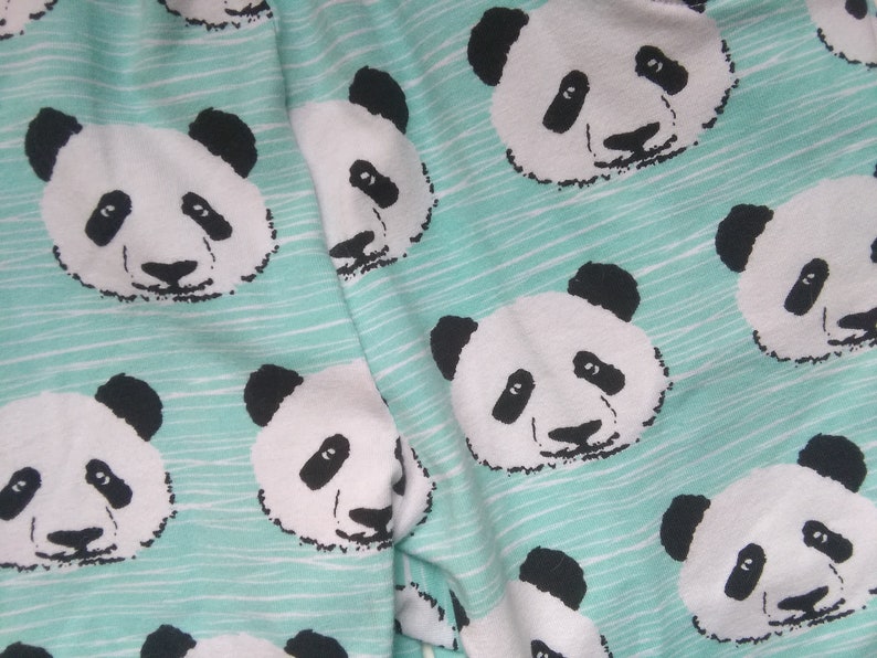 Op de afbeelding: Een turquoise stof met een herhalend patroon van zwart-witte panda gezichten.