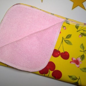 Op de afbeelding: Een roze en gele baby spuugdoek met een kersenprint. De ene kant is roze badstof en de andere kant is gele katoen met een kersenprint.