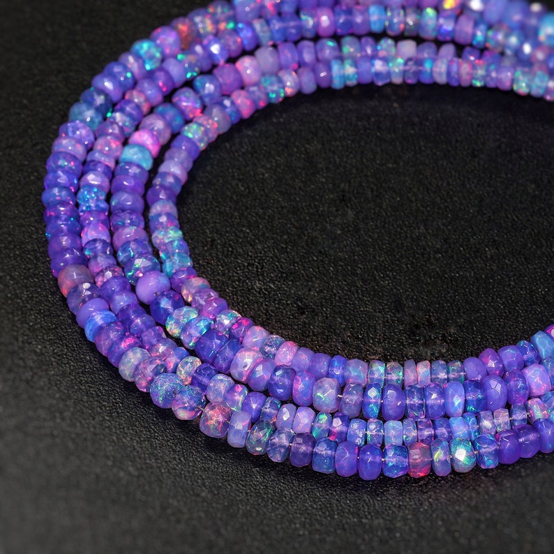 May include: A strand of purple opal beads with iridescent shimmer. The beads are faceted and have a rounded shape. The beads are strung on a clear thread and are arranged in a circular pattern.