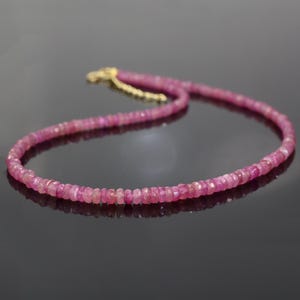 May include: A delicate pink sapphire beaded necklace with a gold clasp. The necklace is made of small, round beads that are strung together on a thin chain.