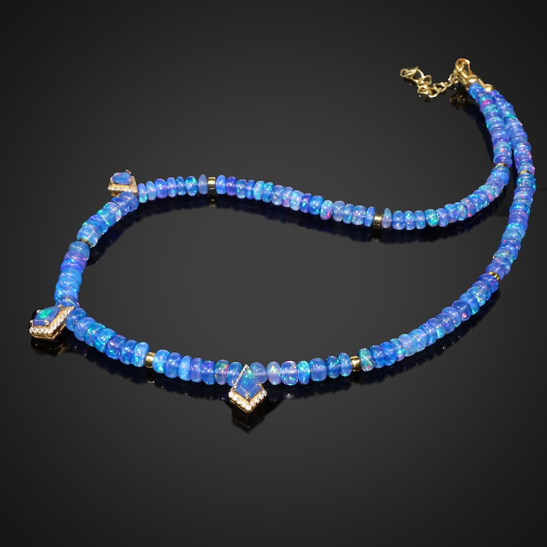 May include: A blue opal gemstone necklace with gold accents. The necklace features a series of small, round blue opals strung together with gold beads. There are three larger, square-shaped blue opals with gold settings hanging from the necklace.