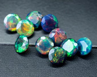 May include: A collection of round, iridescent opal gemstones in various shades of green, blue, and red. The gemstones are faceted and have a shiny, reflective surface.