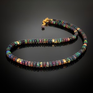 May include: A black opal beaded necklace with gold accents. The necklace is made of small, round beads that are strung together on a gold chain. The beads are a variety of colors, including black, green, blue, and purple.