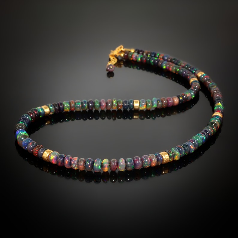 May include: A black opal beaded necklace with gold accents. The necklace is made of small, round beads that are strung together on a gold chain. The beads are a variety of colors, including black, green, blue, and purple.