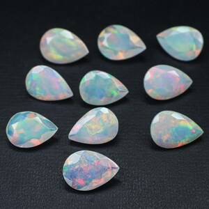 May include: Ten pear-shaped opals with iridescent colors, ranging from white to green and blue, are arranged on a black surface.
