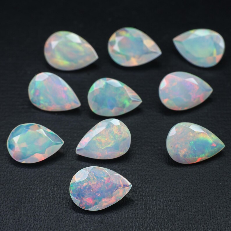 May include: Ten pear-shaped opals with iridescent colors, ranging from white to green and blue, are arranged on a black surface.