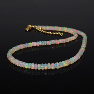 May include: A delicate necklace made of iridescent white opal beads. The necklace is strung on a gold chain and has a simple clasp.