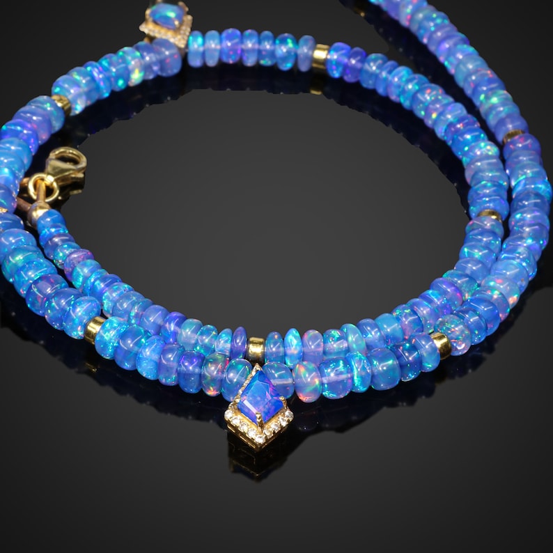 May include: A double strand necklace made of blue opal beads with a gold pendant featuring a blue opal gemstone surrounded by small diamonds.