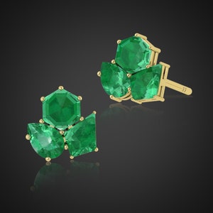 May include: A pair of gold earrings with emerald green gemstones. The earrings feature a cluster of five gemstones, including a hexagonal center stone and four smaller stones.
