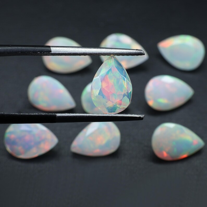 May include: A collection of pear-shaped opals, with one opal held in tweezers. The opals are iridescent and have a milky white color.