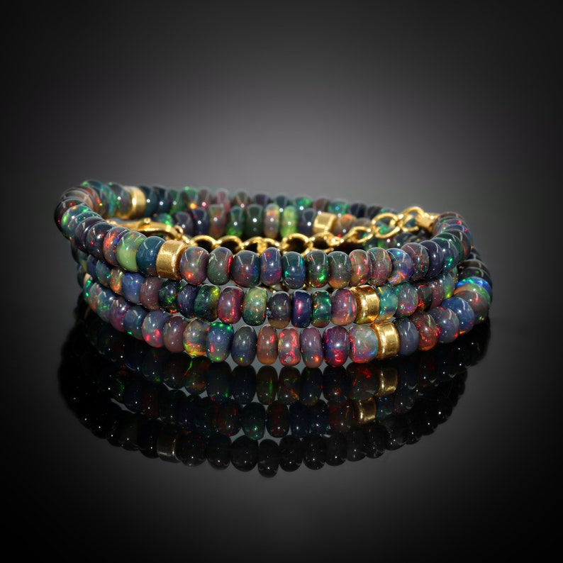 May include: A multi-strand necklace made of black opal beads with gold accents. The necklace is layered and has a reflective surface.