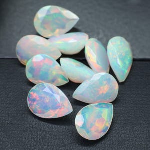 May include: A group of pear-shaped white opals with iridescent rainbow colors. The opals are faceted and have a smooth, polished finish.
