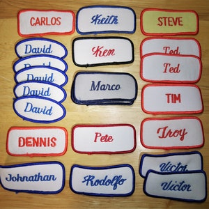 May include: A collection of embroidered patches with various names, including Carlos, Keith, Steve, David, Ken, Ted, Marco, Tim, Troy, Dennis, Pete, Johnathan, Rodolfo, and Victor. The patches are white, yellow, red, and blue with black and gray accents.