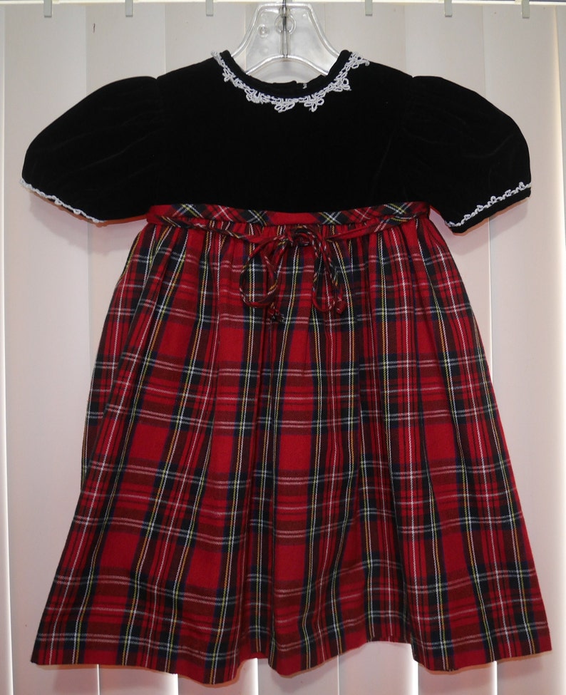 This is a classic Red plaid dress with the sleeves and upper chest of dressing Black Velvet with white lace trim around crew neckline and short puffed sleeves. A very classic child's formal dress for any special occasion.