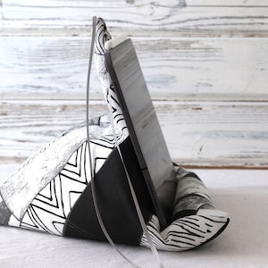 Könnte beinhalten: Ein dreieckiger Kissenständer mit schwarz-weißem Muster, auf dem ein schwarzes Tablet aufgestellt ist. Der Ständer ist aus Stoff.