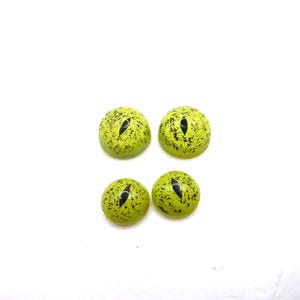 Op de afbeelding: Vier ronde cabochons met een heldere limoengroene basiskleur, zwarte spikkelpatronen en een verticale zwarte spleetpupil in het midden, die doen denken aan reptielen- of kattenogen. Deze gladde, ronde voorwerpen hebben een glanzende afwerking.