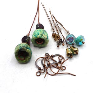 May include: A collection of handmade jewellery components, including two green and blue bell-shaped beads, various beaded headpins, and several pairs of copper-coloured earring hooks. The beads have a textured appearance.