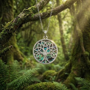 May include: A silver pendant necklace with a circular pendant showcasing a Celtic tree of life design. The pendant has a mother-of-pearl background and a small, clear gemstone. The necklace is suspended from a silver chain.