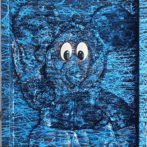 May include: A blue and black framed artwork featuring a 3D sculpture of a cartoon character with large eyes. The sculpture is painted in shades of blue and black, and the background is covered in blue paint splatters.