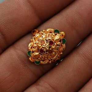 Könnte beinhalten: Ein goldener Ring mit filigranen Details und bunten Edelsteinen. Der Ring hat ein zentrales Design mit einem Sternmuster und ist mit grünen, roten und orangefarbenen Steinen verziert.