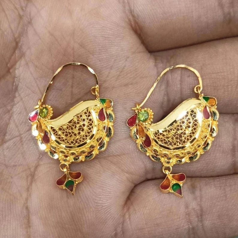 May include: A pair of gold hoop earrings with intricate filigree designs and colorful enamel accents. The earrings feature a teardrop-shaped dangle with a similar design.