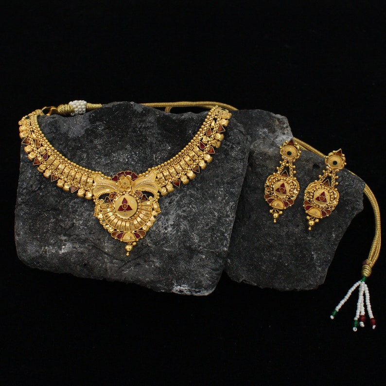 May include: A gold necklace and earrings set with a red and gold pendant. The necklace has a delicate chain and a decorative design. The earrings are drop earrings with a similar design.