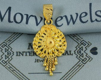 May include: A gold pendant with an intricate filigree design. The pendant has a teardrop shape in the center, surrounded by a circular pattern. Small gold beads hang from the bottom. The pendant is likely made of gold.