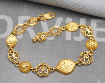 Puede incluir: Una pulsera dorada con varios eslabones decorativos. La pulsera presenta una mezcla de formas, incluyendo eslabones ovalados, redondos y en forma de diamante, con intrincados diseños calados y superficies texturizadas. El cierre es visible en la parte superior.