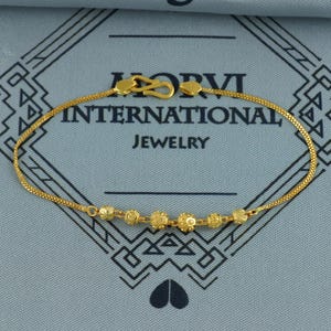 May include: A gold-colored bracelet with a delicate chain and a series of decorative beads. The bracelet features a hook clasp and is displayed against a gray background with the text "HORVI INTERNATIONAL JEWELRY".