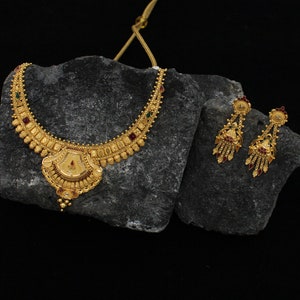 May include: A gold necklace and earrings set with red, green, and white stones. The necklace has a pendant with a decorative design.