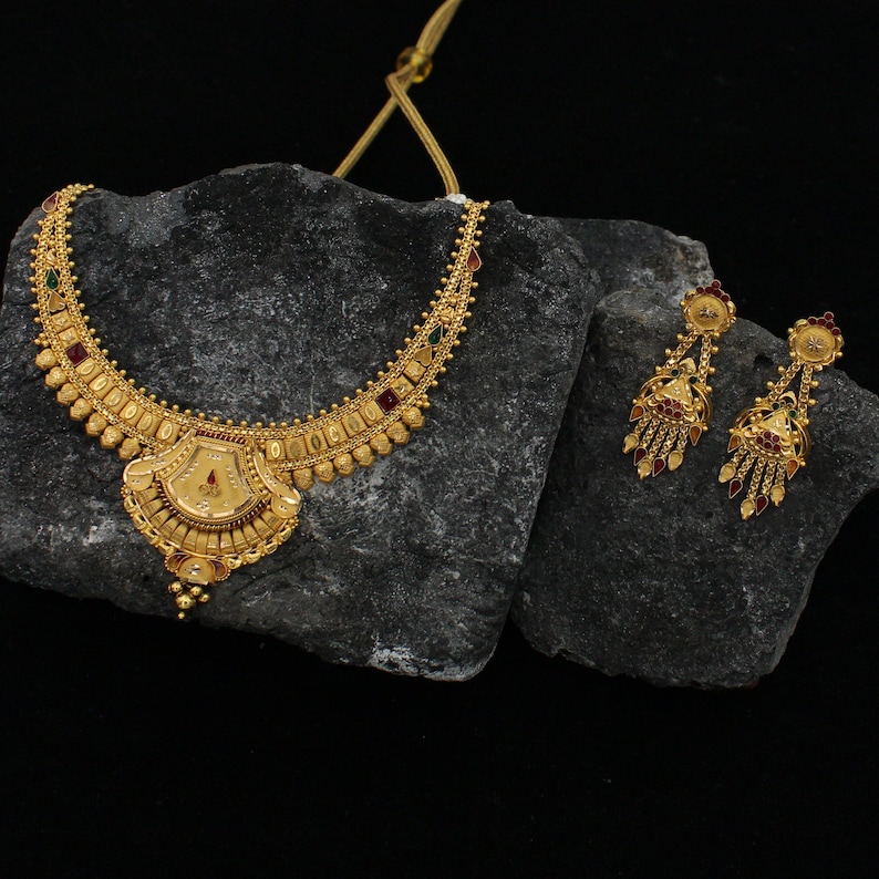 May include: A gold necklace and earrings set with red, green, and white stones. The necklace has a pendant with a decorative design.