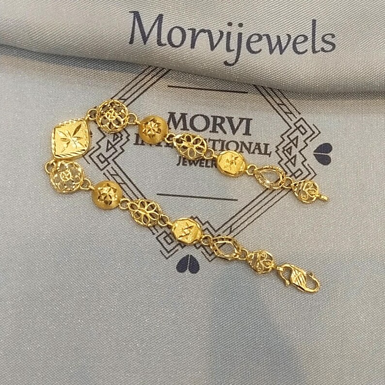 May include: A gold bracelet with intricate designs. The bracelet features a variety of shapes, including squares, circles, and flowers. The bracelet is made of 22 karat gold and is perfect for everyday wear.