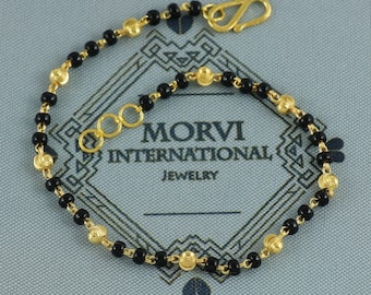 May include: Gold-toned bracelet with black beads and decorative gold accents. The bracelet features a hook clasp and three small connecting rings. The text "MORVI INTERNATIONAL JEWELRY" is visible in the background.