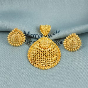 Op de afbeelding: Een gouden kettingset met hanger en bijpassende oorbellen. De hanger is rond en heeft een getextureerd ontwerp. De oorbellen zijn klein en rond met een vergelijkbaar getextureerd ontwerp.