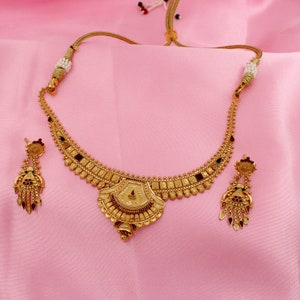 May include: A gold necklace with a pendant and matching earrings. The necklace has a decorative design with red and green stones. The earrings are dangle style with red and green stones.