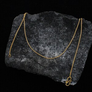 May include: A gold chain necklace with a box clasp. The chain is on a dark gray rock surface.