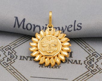 May include: A gold pendant featuring a sun design with a face at the center, surrounded by stylized rays. The pendant is suspended from a small loop. The background includes the text "Mon Jewels INTERNATIONAL JEWELRY".
